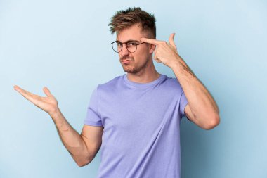 Kafkasyalı genç adam mavi arka planda izole edilmiş ve elinde bir ürün tutuyor..