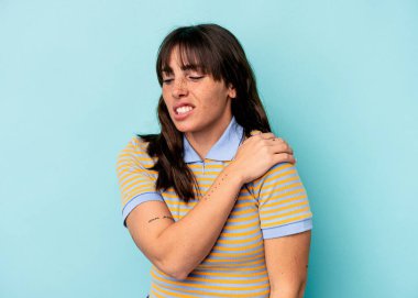 Arjantinli genç bir kadın mavi arka planda izole edilmiş, omuz ağrısı var..