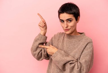 Mavi arka planda izole edilmiş genç beyaz kadın işaret parmağıyla fotokopi alanını işaret ederek şok oldu..