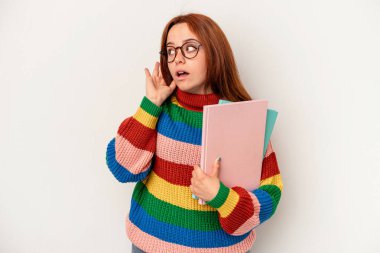 Young student caucasian woman isolated on white background trying to listening a gossip.