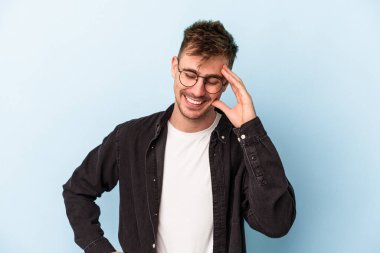 Kafkasyalı genç adam mavi arka planda izole edilmiş neşeli bir şekilde gülüyor. Mutluluk kavramı.