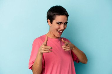 Mavi arka planda izole edilmiş genç beyaz kadın parmaklarıyla ön tarafı işaret ediyor..