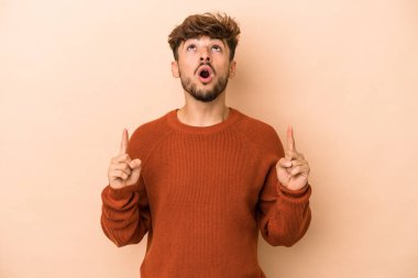 Young arab man isolated on beige background pointing upside with opened mouth.