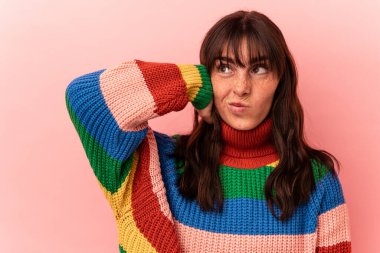 Arjantinli genç bir kadın pembe arka planda izole edilmiş kafasının arkasına dokunuyor, düşünüyor ve bir seçim yapıyor..