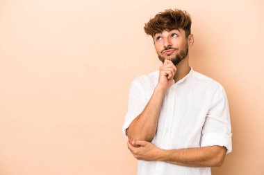 Young arab man isolated on beige background relaxed thinking about something looking at a copy space.
