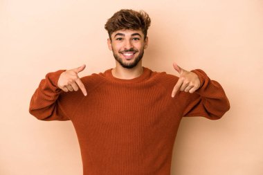 Genç Arap adam bej arka planda izole edilmiş. Parmakları aşağıda, olumlu hisler var..