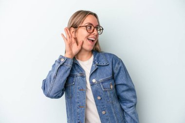 Mavi arka planda izole edilmiş genç beyaz kadın bir dedikoduyu dinlemeye çalışıyor..