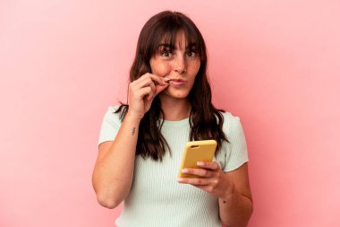 Pembe arka planda cep telefonu tutan Arjantinli genç bir kadın. Parmakları dudaklarında bir sır saklıyor..
