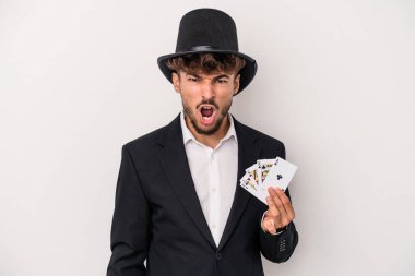 Young arab wizard man holding a magic cards isolated on white background screaming very angry and aggressive.