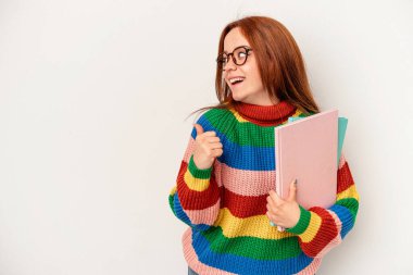 Young student caucasian woman isolated on white background points with thumb finger away, laughing and carefree.