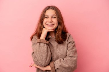 Küçük beyaz kız pembe arka planda izole edilmiş mutlu ve kendinden emin gülümsüyor, elleriyle çenesine dokunuyor..