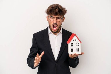 Young arab real estate man holding a model house isolated on isolated background screaming very angry and aggressive.