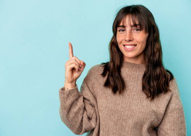 Arjantinli genç bir kadın mavi arka planda izole edilmiş. Parmağıyla bir numarayı gösteriyor..