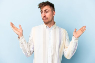 Kafkasyalı genç adam mavi arka planda izole edilmiş. Kafası karışmış ve omuz silkiyor. Kopya alanını tutmak için..