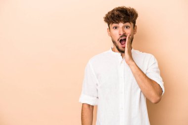 Young arab man isolated on beige background shouts loud, keeps eyes opened and hands tense.