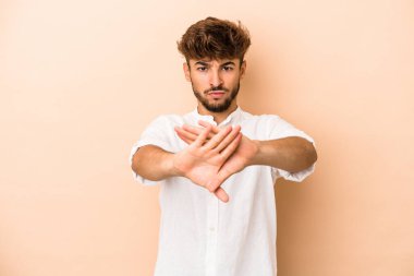 Young arab man isolated on beige background standing with outstretched hand showing stop sign, preventing you.