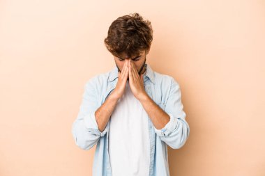 Young arab man isolated on beige background praying, showing devotion, religious person looking for divine inspiration.