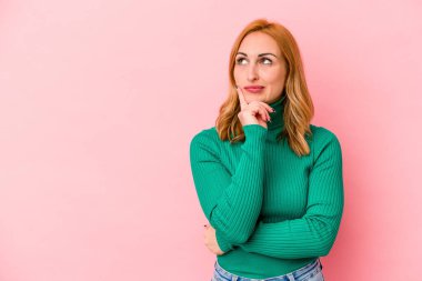 Pembe arka planda soyutlanmış beyaz bir kadın şüpheli ve şüpheci bir ifadeyle yana bakıyor..