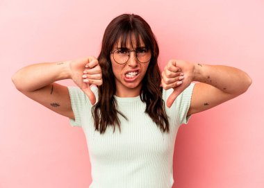 Pembe arka planda izole edilmiş genç Arjantinli kadın baş parmağını aşağı gösteriyor ve hoşlanmadığını ifade ediyor..
