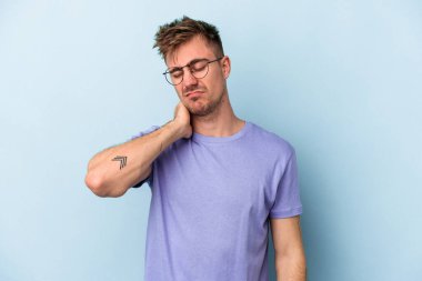 Kafkasyalı genç adam mavi arka planda izole edilmiş. Stres yüzünden boynu ağrıyor. Masaj yapıyor ve elle dokunuyor..