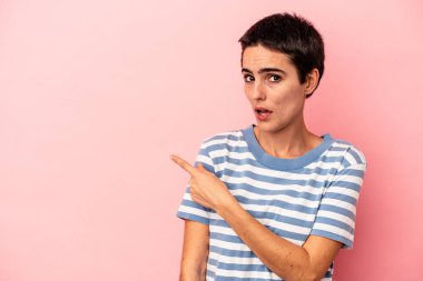 Mavi arka planda izole edilmiş genç beyaz kadın gülümsüyor ve boş alanda bir şeyler gösteriyor..