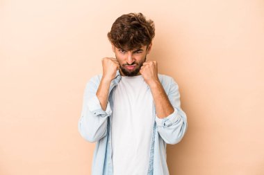 Young arab man isolated on beige background throwing a punch, anger, fighting due to an argument, boxing.