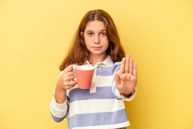 Sarı arka planda izole edilmiş pembe bir kupa tutan küçük beyaz kız elini uzatmış, dur işaretini göstererek seni engelliyor..