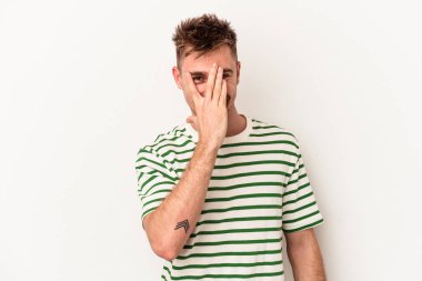 Beyaz arka planda izole edilmiş genç beyaz bir adam kameraya parmaklarıyla göz kırpıyor, yüzünü kapatmaktan utanıyor..