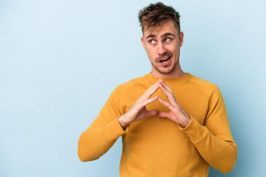 Kafkasyalı genç bir adam mavi arka planda izole edildi. Aklında bir plan kuruyor, bir fikir kuruyor..