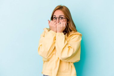 Mavi arka planda izole edilmiş, tırnak yiyen, gergin ve endişeli bir beyaz kadın..