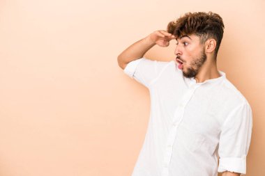 Young arab man isolated on beige background looking far away keeping hand on forehead.