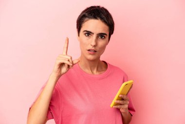 Elinde cep telefonu olan beyaz bir kadın pembe arka planda izole edilmiş. Bir fikri, ilham verici bir fikri var..
