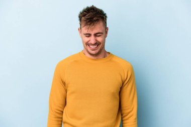 Mavi arka planda izole edilmiş genç beyaz adam gülüyor ve gözlerini kapıyor, rahatlamış ve mutlu hissediyor..