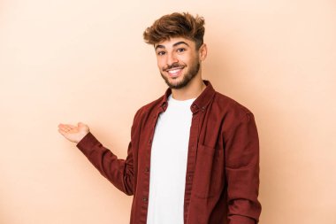 Young arab man isolated on beige background showing a welcome expression.