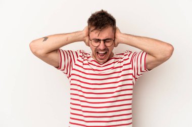 Beyaz arka planda izole edilmiş genç beyaz bir adam kulakları kulaklarıyla kapatıyor ve çok ses duymamaya çalışıyor..