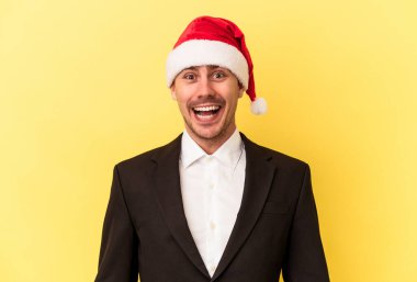 Yeni yılı kutlayan beyaz bir genç adam sarı arka planda izole edilmiş bir Noel şapkası takıyor.