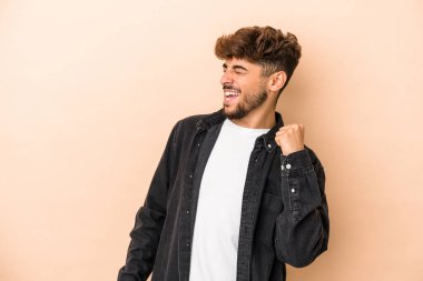 Young arab man isolated on beige background celebrating a victory, passion and enthusiasm, happy expression.