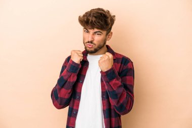 Young arab man isolated on beige background showing fist to camera, aggressive facial expression.