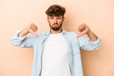 Young arab man isolated on beige background showing a dislike gesture, thumbs down. Disagreement concept.