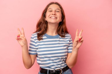 Pembe arka planda izole edilmiş küçük beyaz kız zafer işareti gösteriyor ve gülümsüyor..