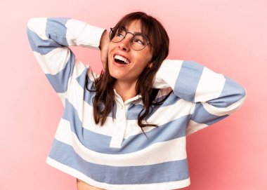 Arjantinli genç bir kadın pembe arka planda izole edilmiş, kendinden emin, elleri başının arkasında..