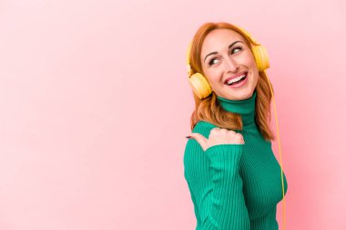 Pembe arka planda müzik dinleyen beyaz bir kadın. Baş parmak uzakta, gülüyor ve kaygısız..