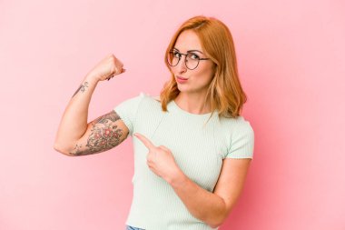 Pembe arka planda izole edilmiş genç beyaz kadın güçlü bir hareket gösteriyor. Kollarıyla, kadınsı gücün sembolü.