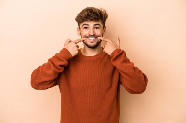 Young arab man isolated on beige background smiles, pointing fingers at mouth.