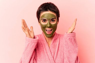 Pembe arka planda soyutlanmış yüz maskesi takan beyaz bir kadın hoş bir sürprizle karşılaşıyor, heyecanlı ve el kaldırıyor..