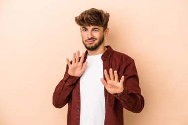Young arab man isolated on beige background rejecting someone showing a gesture of disgust.