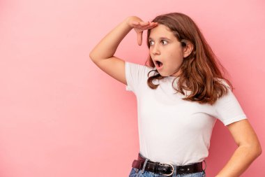 Pembe arka planda izole edilmiş küçük beyaz kız uzaklara bakıyor ve elini alnına koyuyor..
