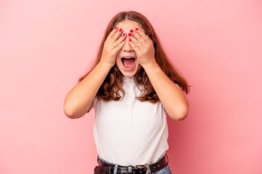 Pembe arka planda izole edilmiş küçük beyaz kız elleriyle gözlerini kapatıyor, gülümseyerek bir sürpriz bekliyor..