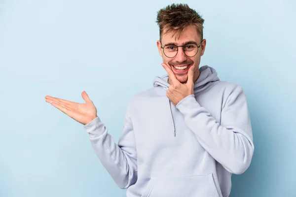 Young Caucasian Man Isolated Blue Background Holds Copy Space Palm — Stock Photo, Image