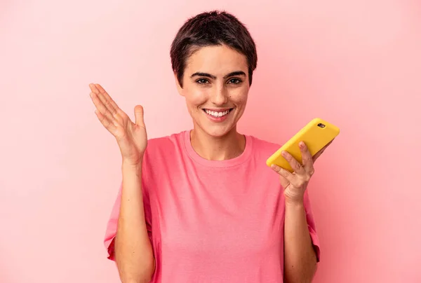 ピンクの背景に隔離された携帯電話を持っている若い白人女性は 楽しい驚き 興奮し 手を上げる — ストック写真